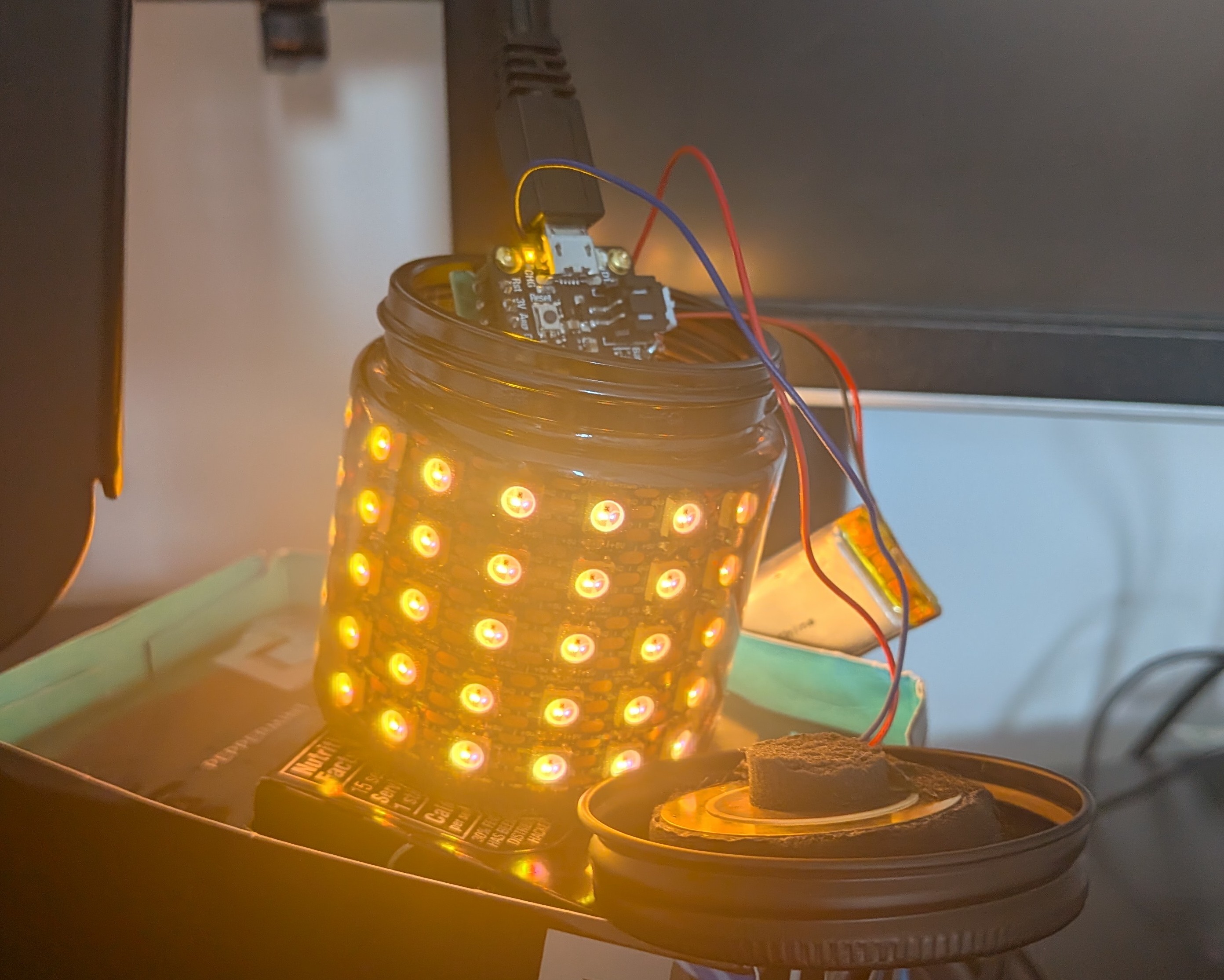 The LED matrix fitted inside the jar with the Feather board, battery, and piezo touch sensor connected